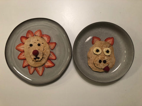 Plates with food art of a pig and lion made out of pancakes and fruit