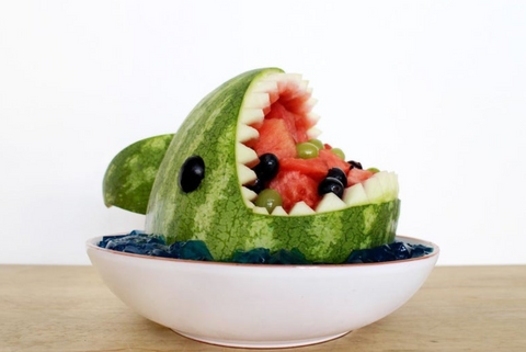 Watermelon cut into the shape of a shark with watermelon chunks and grapes in the mouth