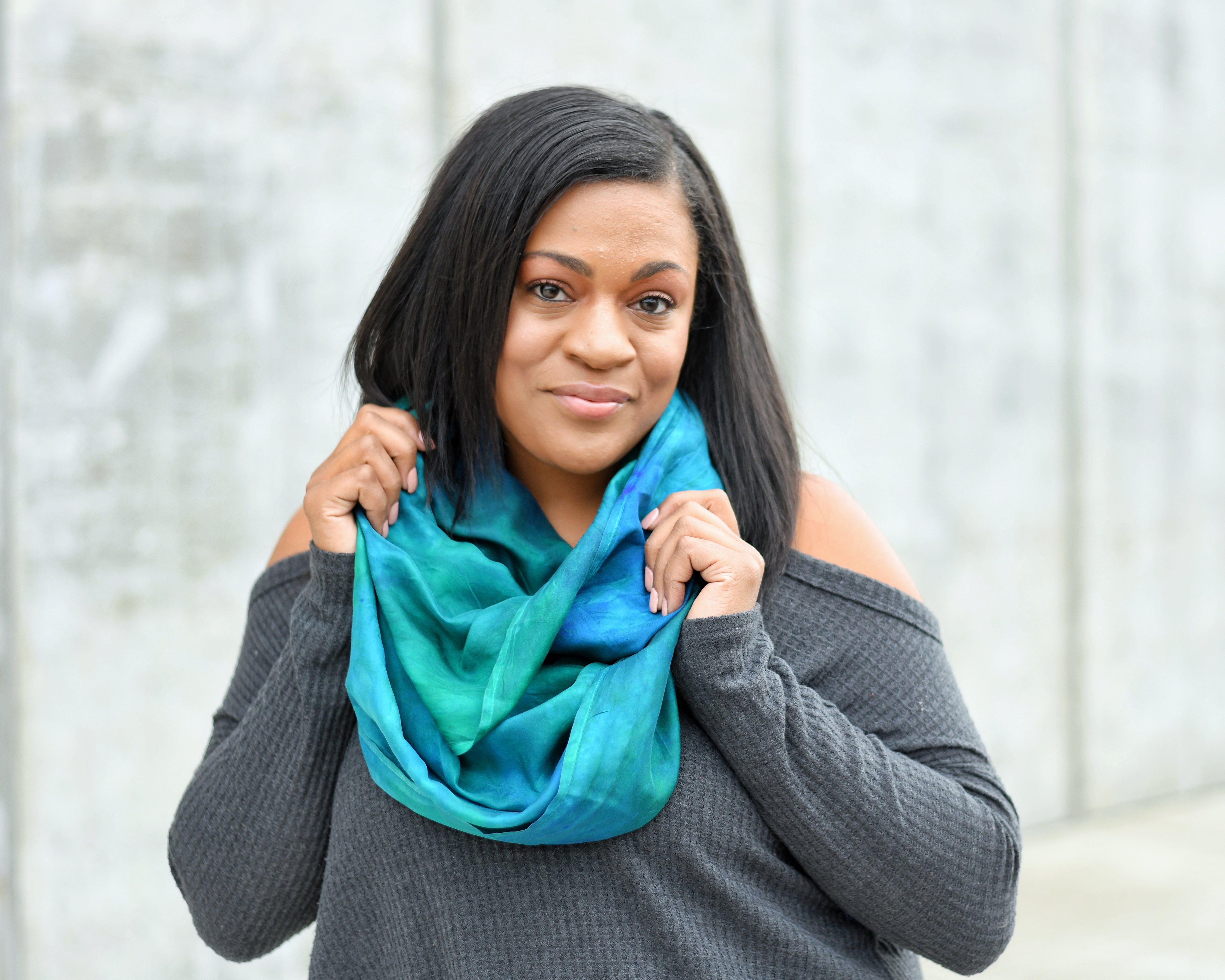 Black woman outside by an off white wall, wearing a green silk scarf