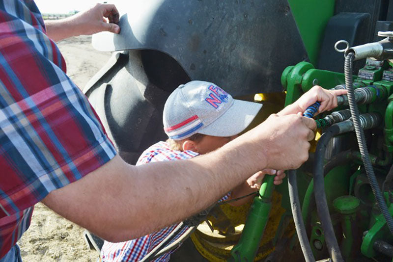 A father and son install outback wrap hydraulic hose markers on their tractor