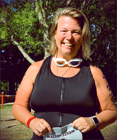 Lisa H. JunoActive customer smiling at the camera wearing a JunoActive Aquatard holding a swim cap in her hands. Outside on a bright sunny day.