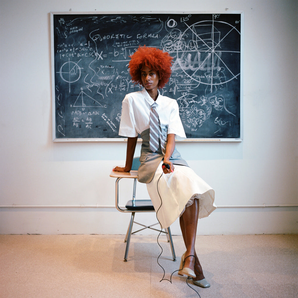 stunning model seated on top of desk in front of chalk board.