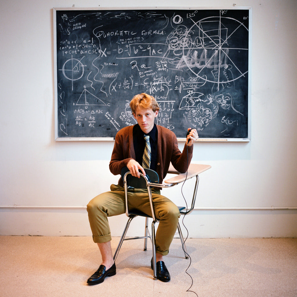 model sitting in desk backwards in front of chalkboard.