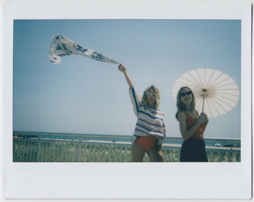 two models in red white and blue on the boardwalk with the beach behind them. 