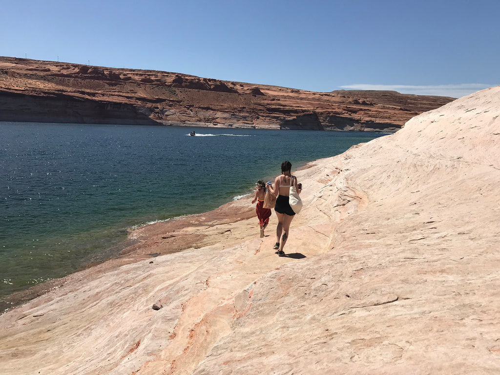 two people walking on a rocky path near a body of water.