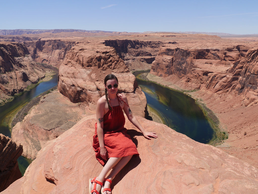 a person in a red dress sitting on a cliff overlooking a river.