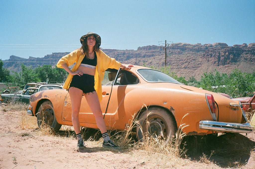 person posing next to a yellow old volkswagen.