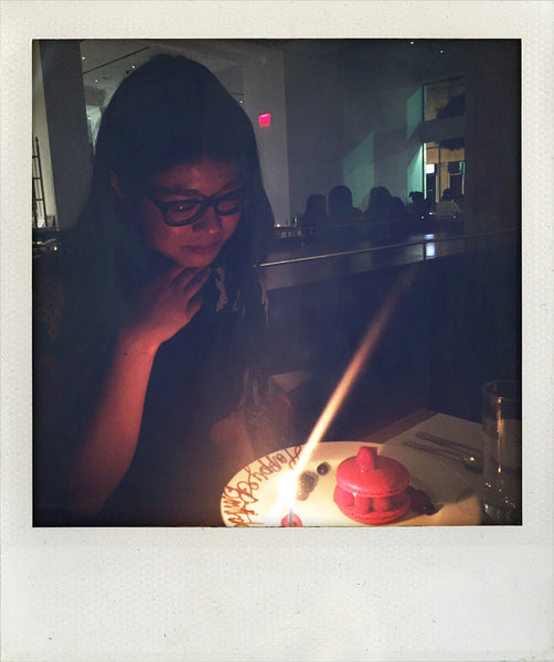 polaroid of a person with light candle on a cake.
