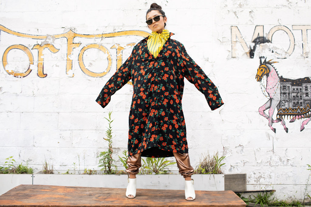 alana murau in striped top and floral print coat standing in front of painted wall.