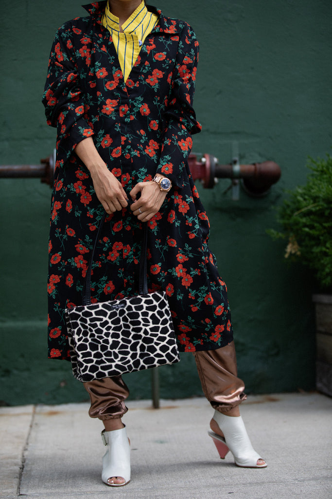 neck-down angle alana murau in front of brick wall with 'kate spade' handbag.