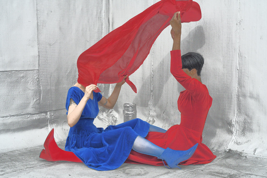 two models sitting facing eachother and interlocking legs with a scarf floating above them.
