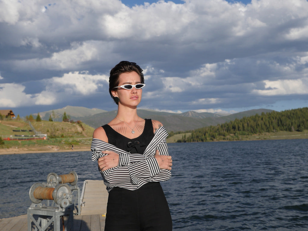 a person with sunglasses is standing on a dock next to a body of water.