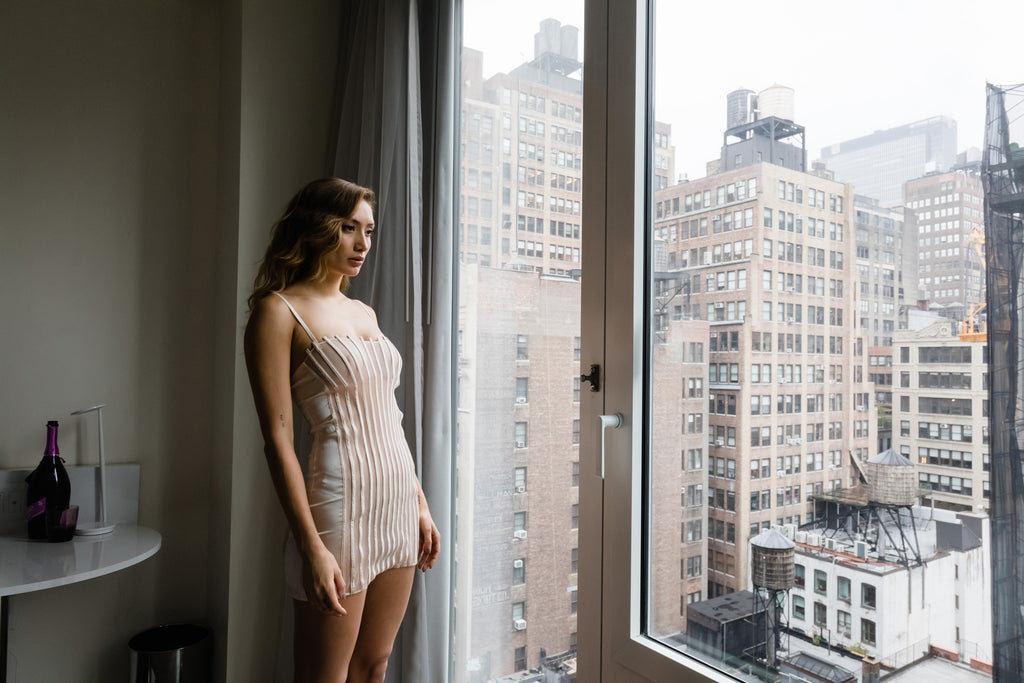 model in la perla lingerie dress looking out a city window at buildings.