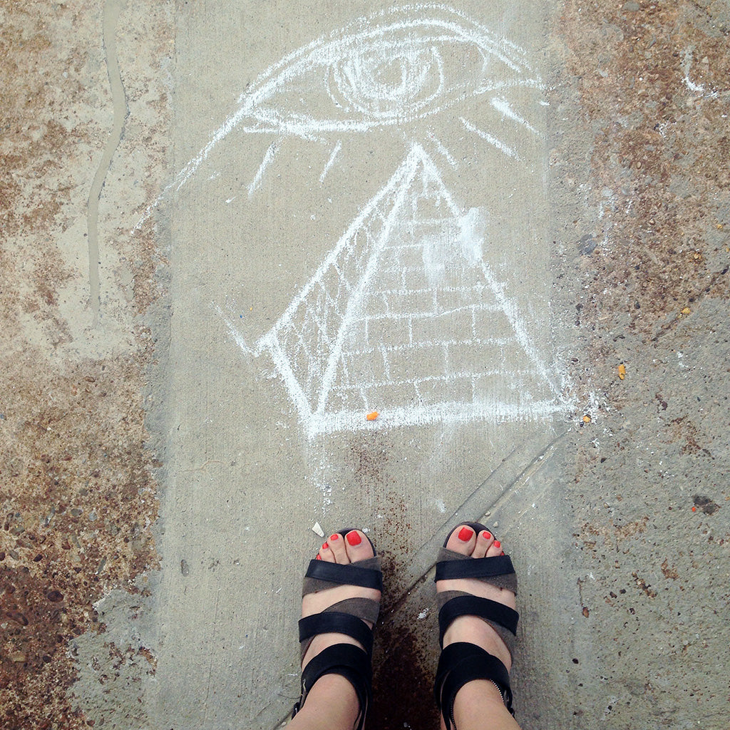 all seeing eye and pyramid in chalk on ground with feet at edge.