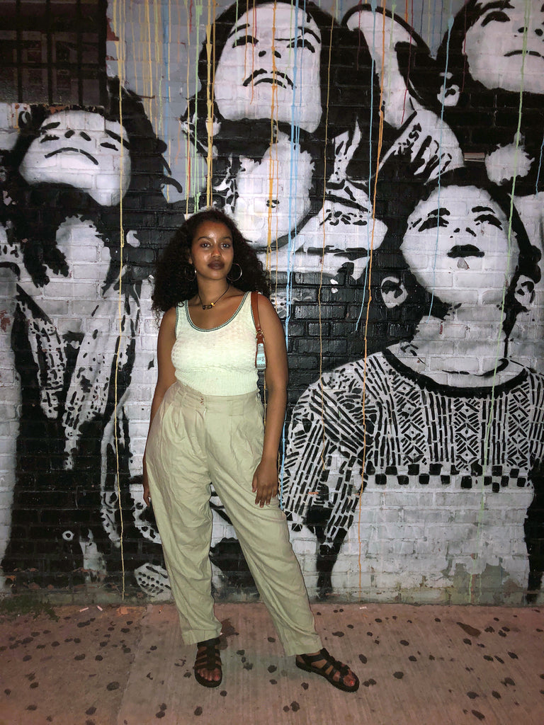 wilhelmina in tank top and pants in front of painted brick wall of faces.