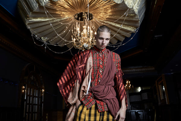 model posing beneath chandelier in tartan layered epic outfit.