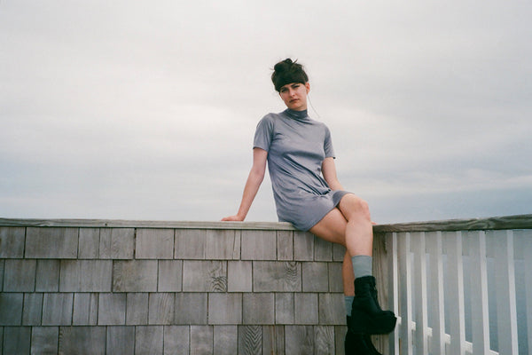 a person in a gray dress sitting on a wooden railing.
