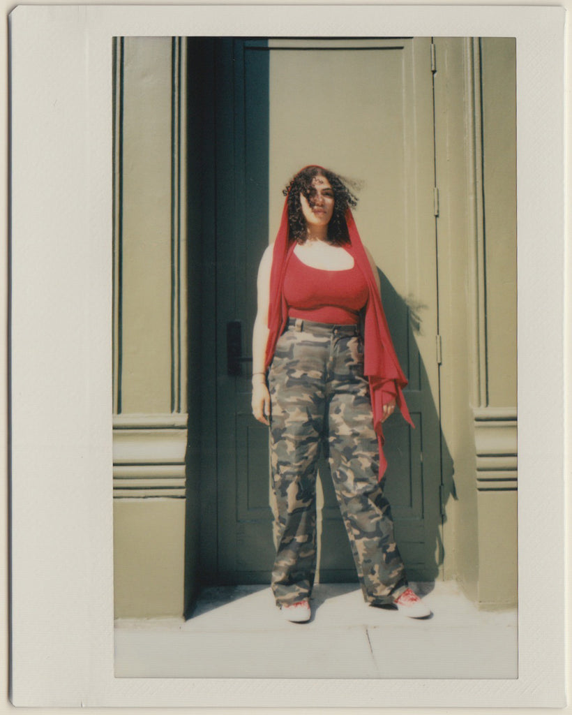 paola in tank and camo pants in front of door.