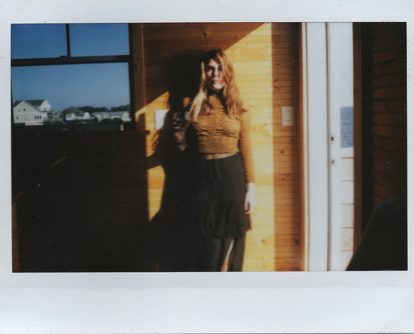 polaroid of a woman standing in front of a wood wall.