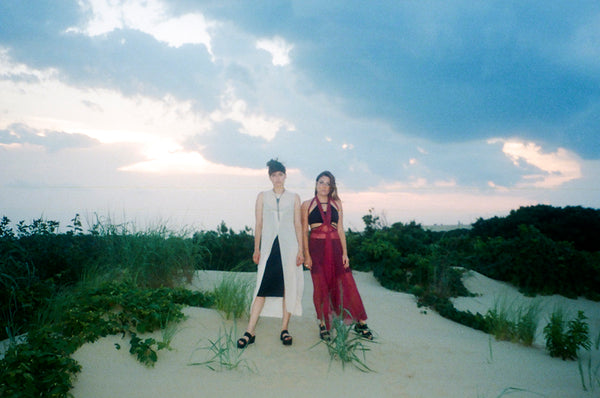 two people standing on a sand dune in front of the ocean.