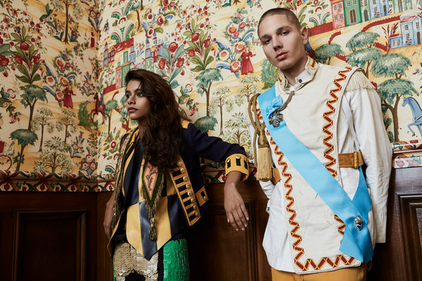 two models posing in model in front of ornate wallpaper in ceremonial regalia and accoutrements.