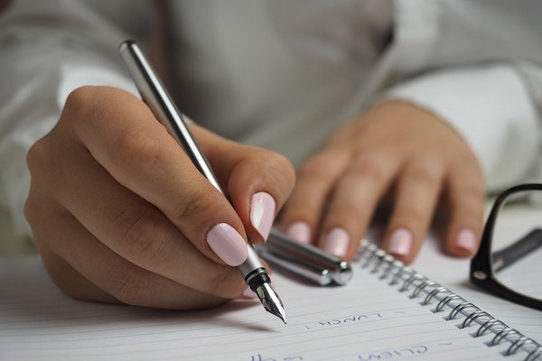 Eve and Elle woman writing in notebook in white blouse with pastel pink nails manicure