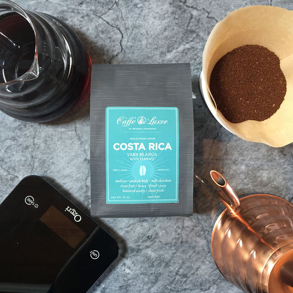 a bag of caffe luxxe costa rica vara blanca surrounded by various coffee brewing equipment