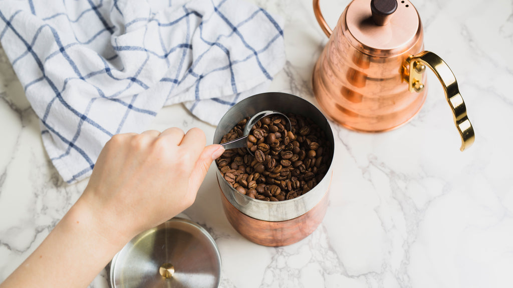 a hand scooping coffee out of copper canister