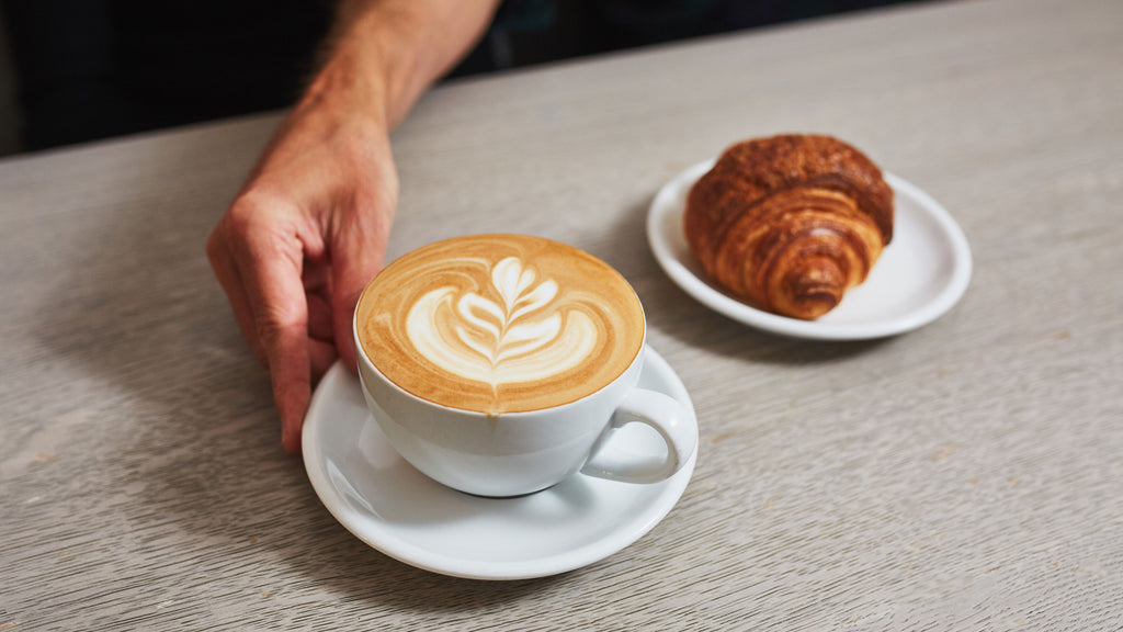 latte with rosetta latte art and croissant on a light grey colored table