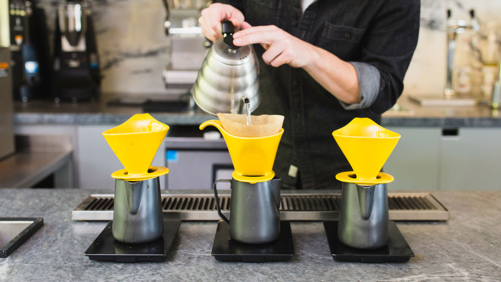 a person making pour over coffee in a yellow bee house dripper