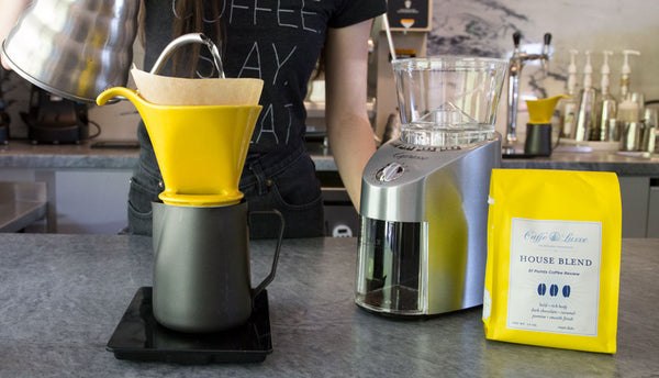 a woman making pour over coffee next to a 
burr grinder and a bag of coffee