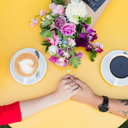 couple holding hands on a yellow table with coffee cups