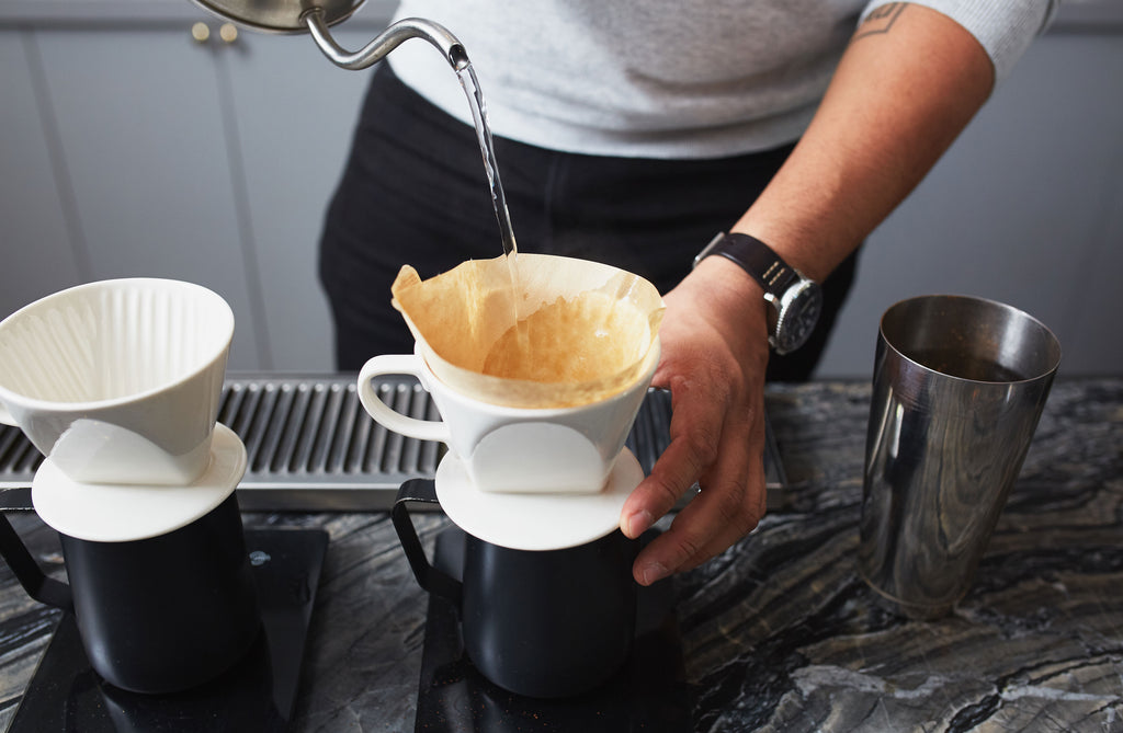 a person prewetting coffee filter with hot water