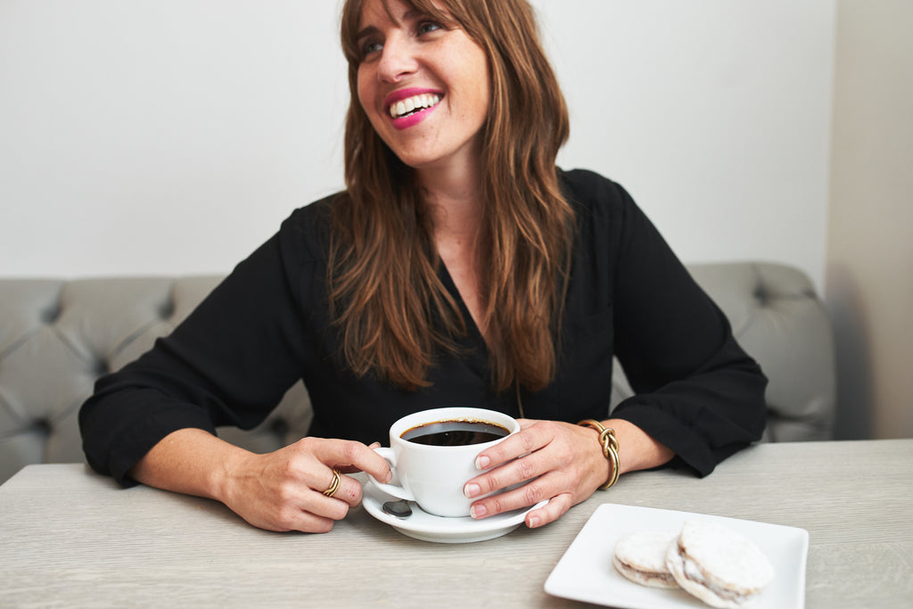 a woman smiling while holding a cup of coffee