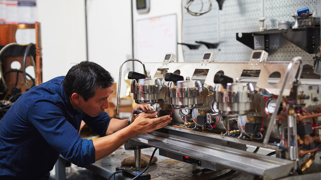 a person in a blue shirt repairing an espresso machine