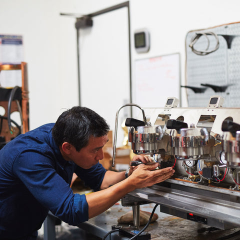 a personin a blue shirt fixing an espresso machine