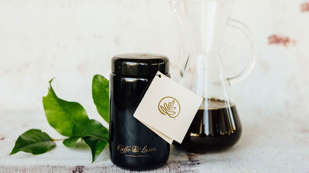 a black canister of caffe luxxe gesha coffee with a chemex behind it