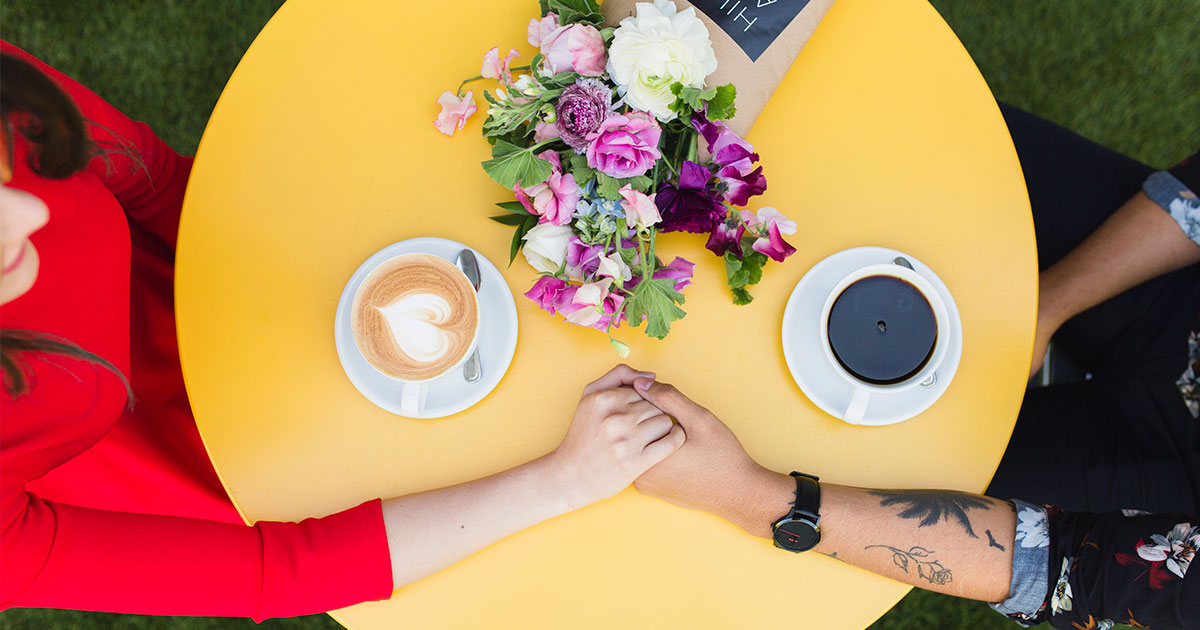 couple holding hands on a yellow table with coffee