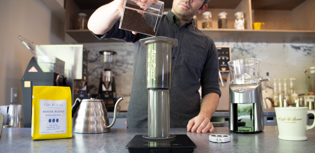a person pouring ground coffee into an aeropress