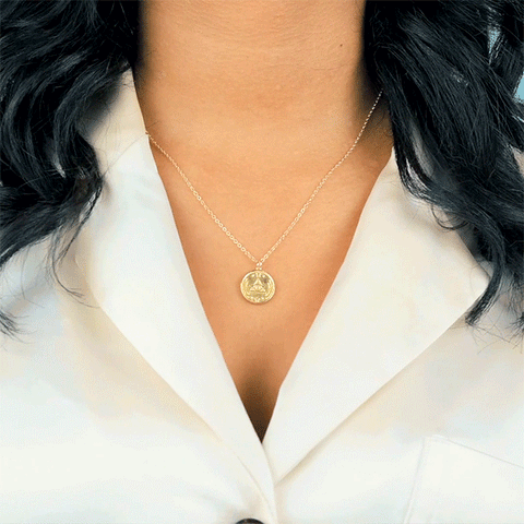 .gif close up up a woman wearing the All Seeing Eye necklace from Katie Dean Jewelry in a pastel yellow top.