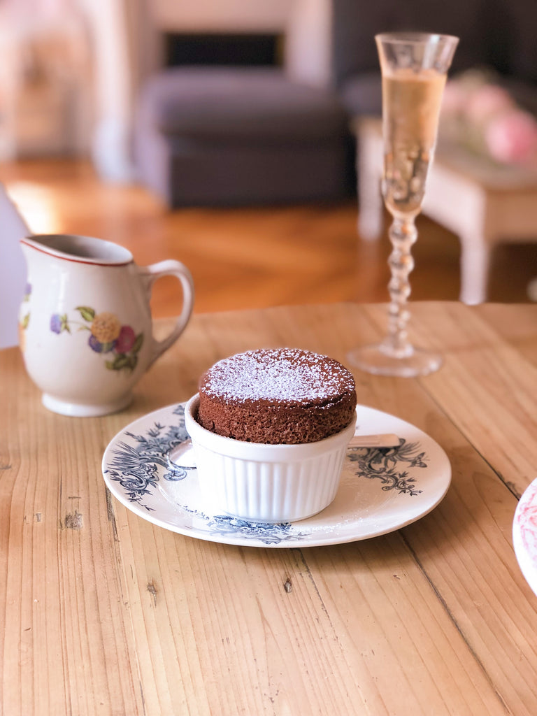 The freshly bakes Chocolate Souffle in a white dish and on top of a vintage plate with blue design. 