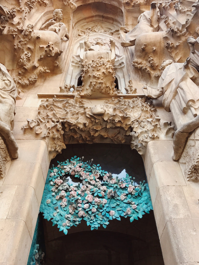 Portion of La Sagrada Familia church in Barcelona Spain with a stone and metal art installation in a archway with green and pink colors showing a rose bush.