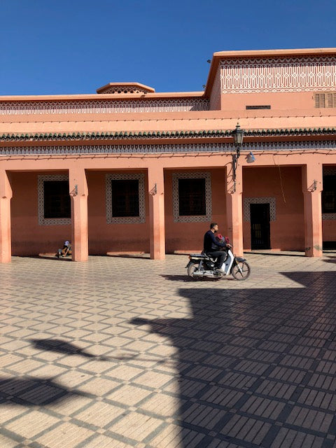 Man on motorcyle on tiled floor in front of salmon colored building. 