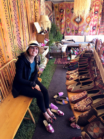 a customer at brimfield antique market choosing between woemsn kilim loafers and womens velvet slides. she is surrounded by kilim carpets and womens and mens kilim loafers.