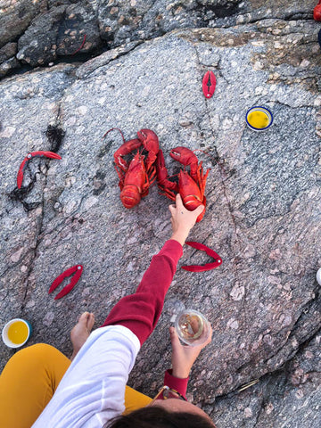 carson in white and yellow, reaching out to lobsters ready to be eaten placed on top of rock. 