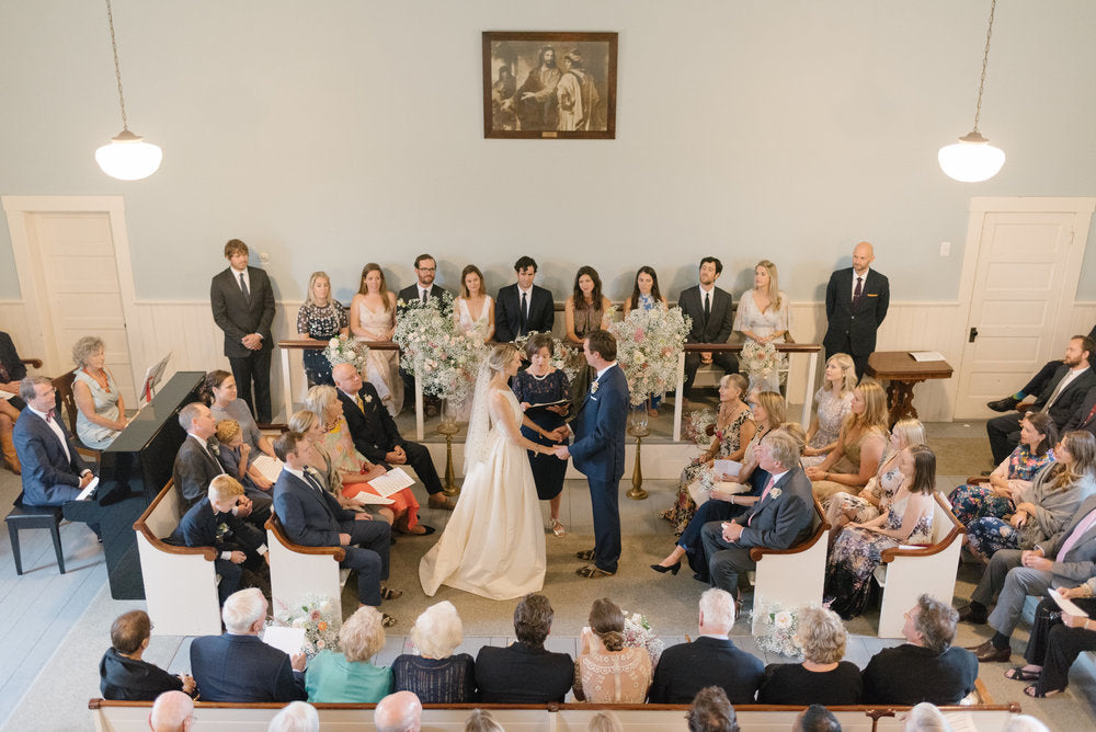 Bride and groom exchanging their vows surrounded by flower arrangements in the church