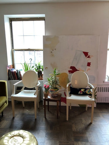 paulines studio with two white chairs, a small brown table between them with a plant and cactus on it. a painting behind the chairs and white walls. 