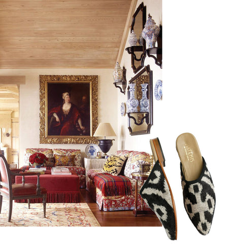 black and white velvet slippers for ibu movement paired with living room scene. living room has red themed assorted couches, painting, and kilim carpet.