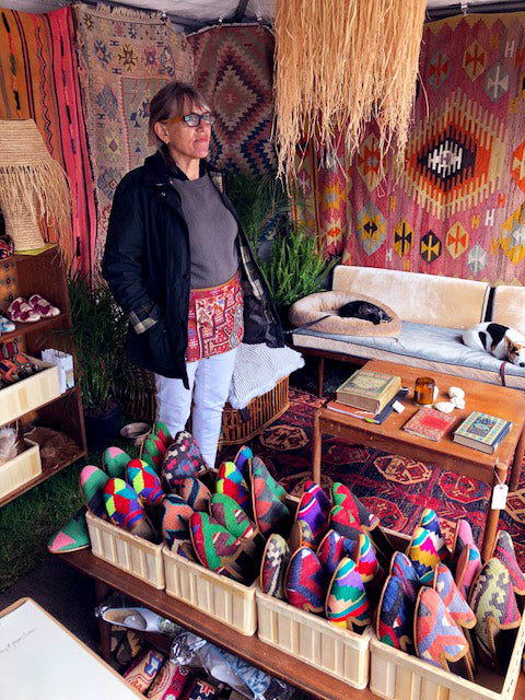 milicents mom preparing for customers surrounded by kilim carpets and standing next to displayed mens kilim loafers and womens kilim loafers.