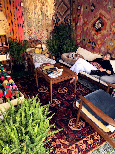 antique carpet books displayed next to silk loafers on table on kilim carpet surrounded by whicker furniture and kilim rugs.